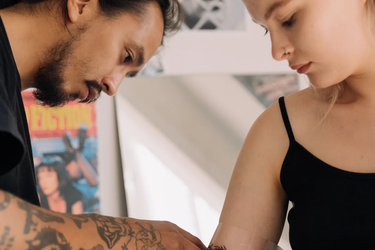 Tattoo artist wrapping a client's fresh arm tattoo, the first step of tattoo aftercare