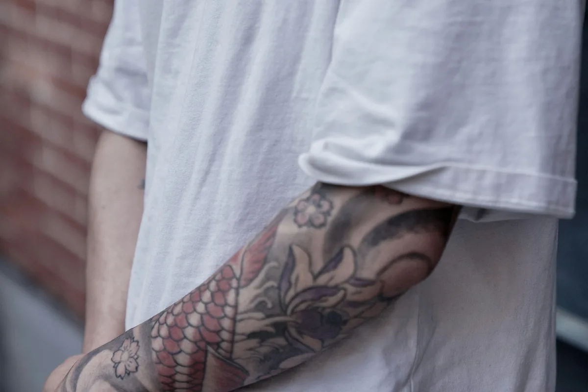Man in a white T-shirt with a black and grey sleeve, the kind of visible tattoo that raises government job questions in Malaysia