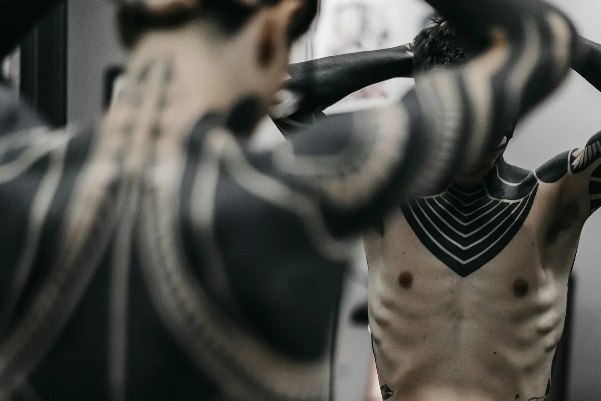 Bold blackwork tattoos across a man's back, arms and torso