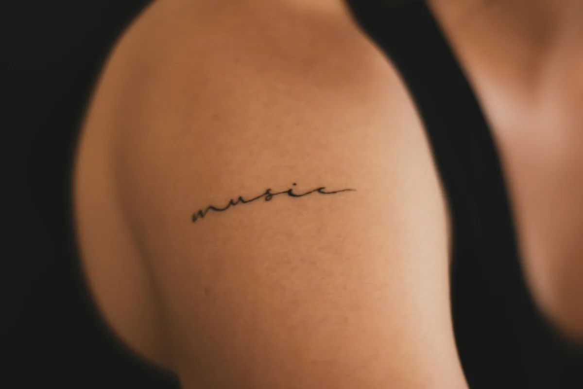 Fine line script tattoo on a shoulder, one of the most popular tattoo styles for a first piece