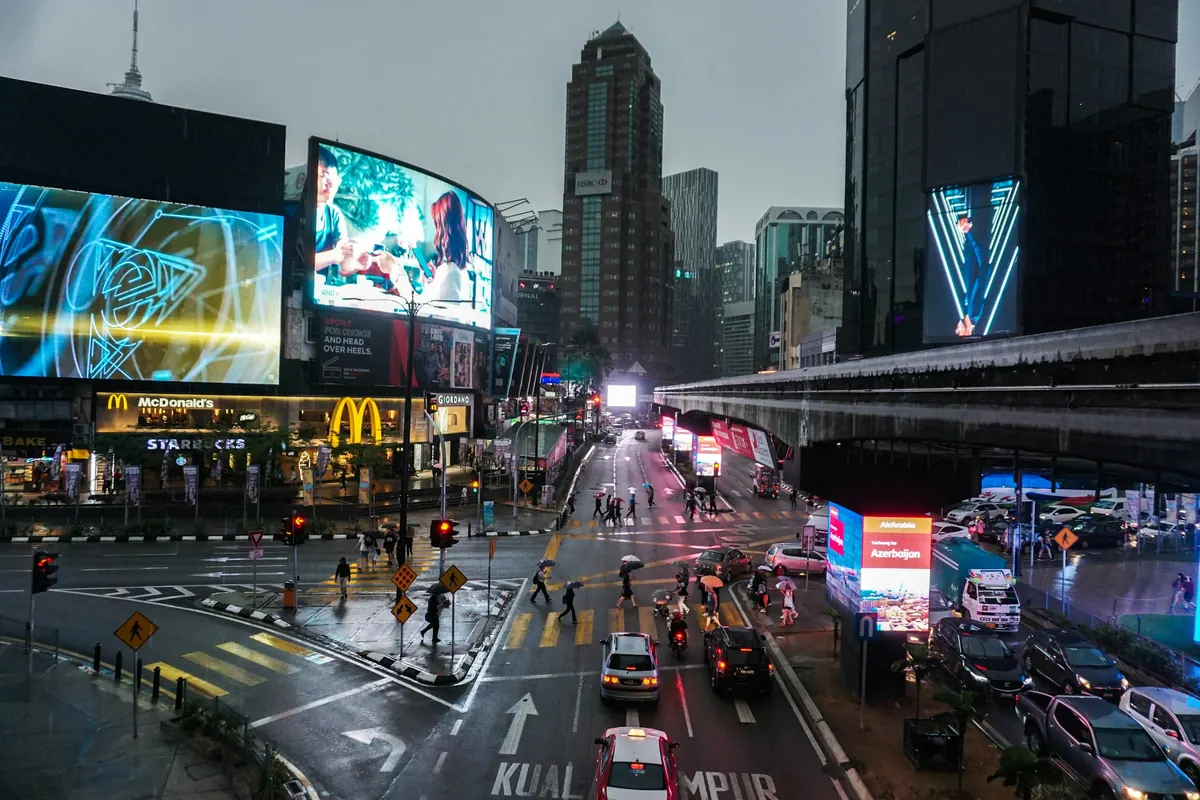 Rainy evening traffic and billboards in central Kuala Lumpur, where many visitors book a tattoo in Malaysia as a tourist