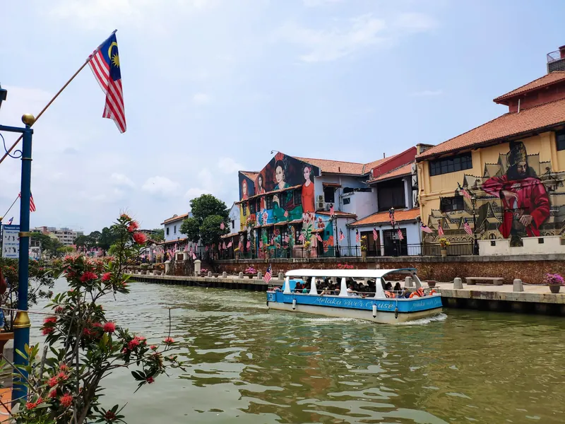 Boat cruising along the Melaka River past murals and old houses