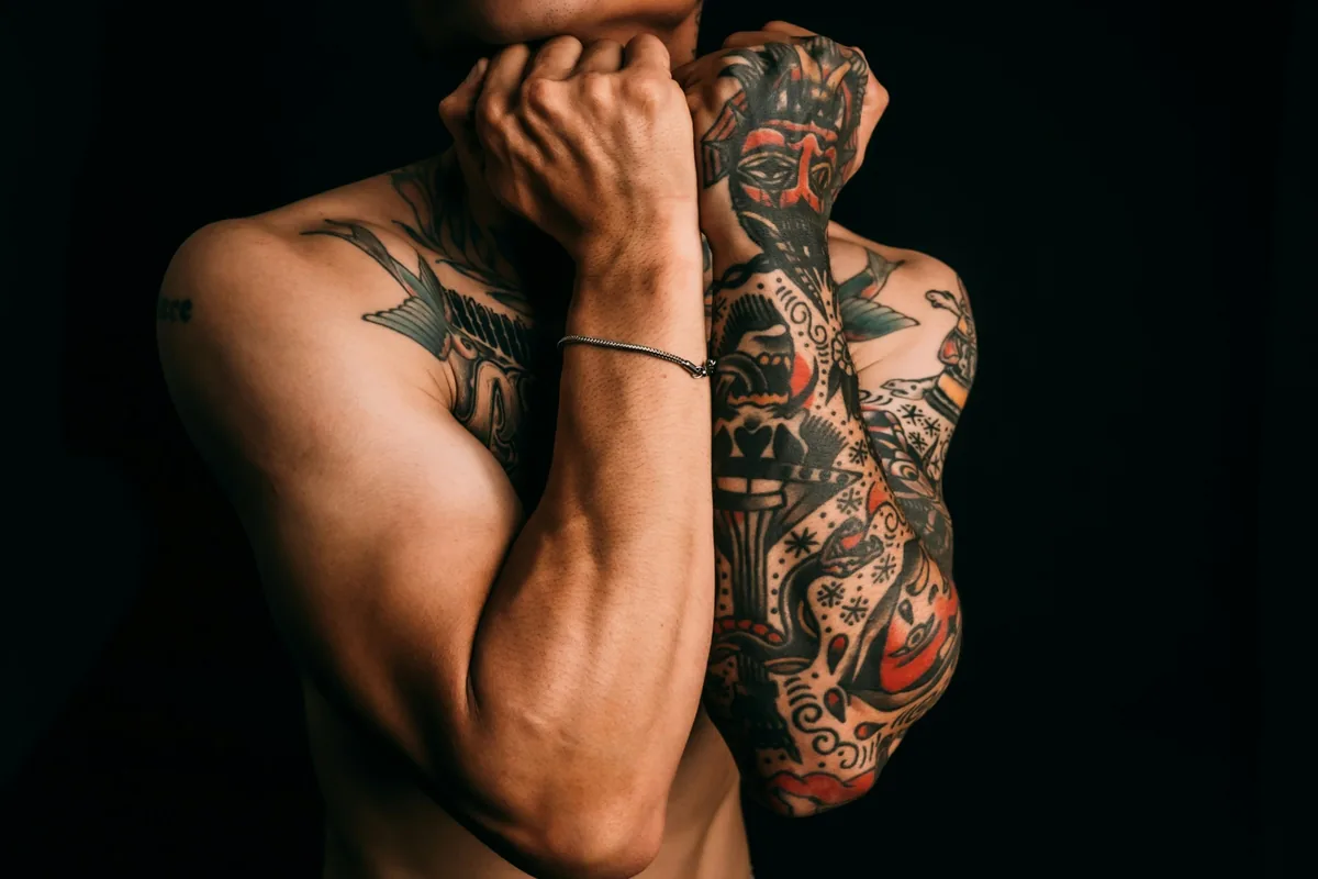 Man with bold colour tattoo sleeves against a black background, an example of classic tattoo designs for men